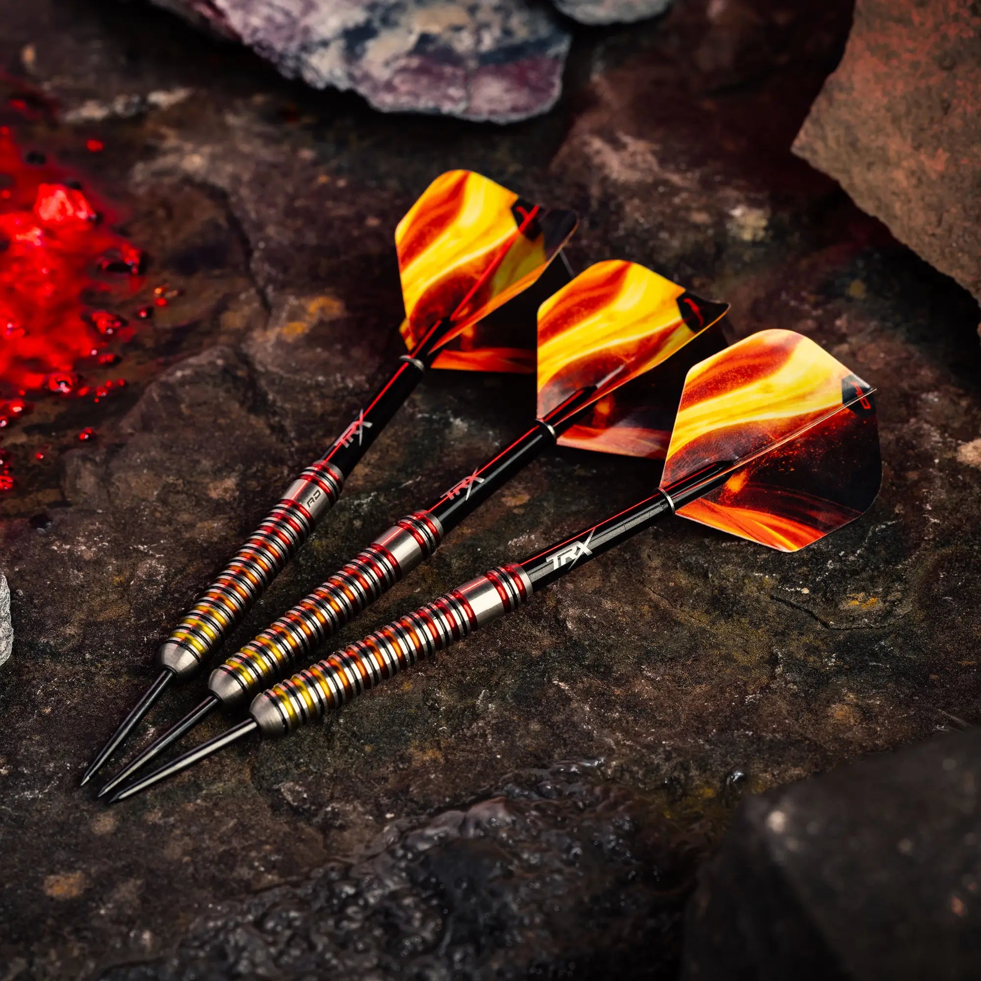 Three Reddragon Furnace darts with metallic striped shafts and yellow, orange, and flame design flights resting on a dark textured stone surface.